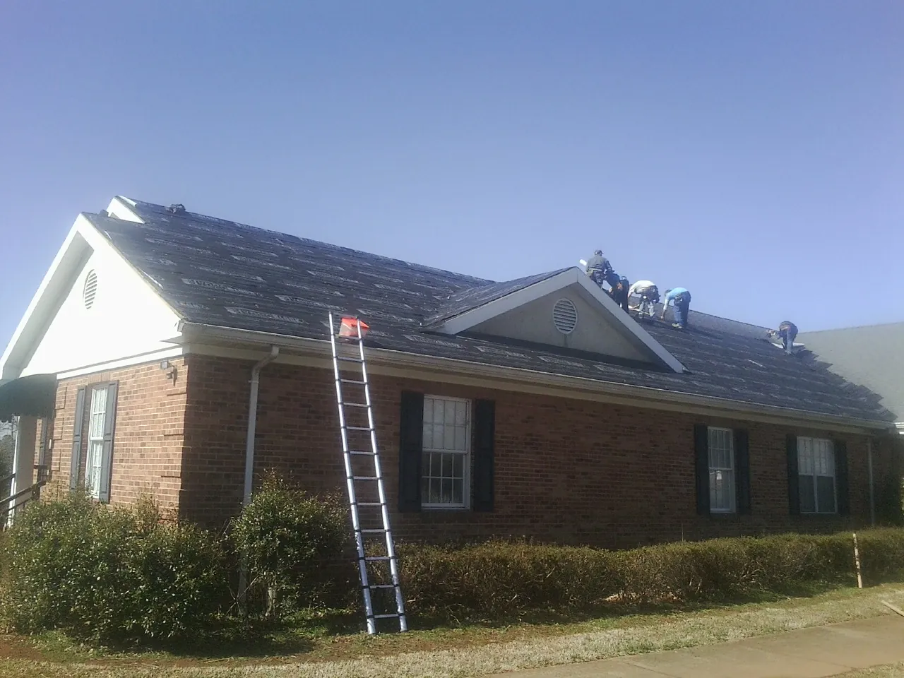 Crew tearing shingles off a brick ranch roof with a ladder set — Emergency Roof Repair work by our crew in Liberty Lake