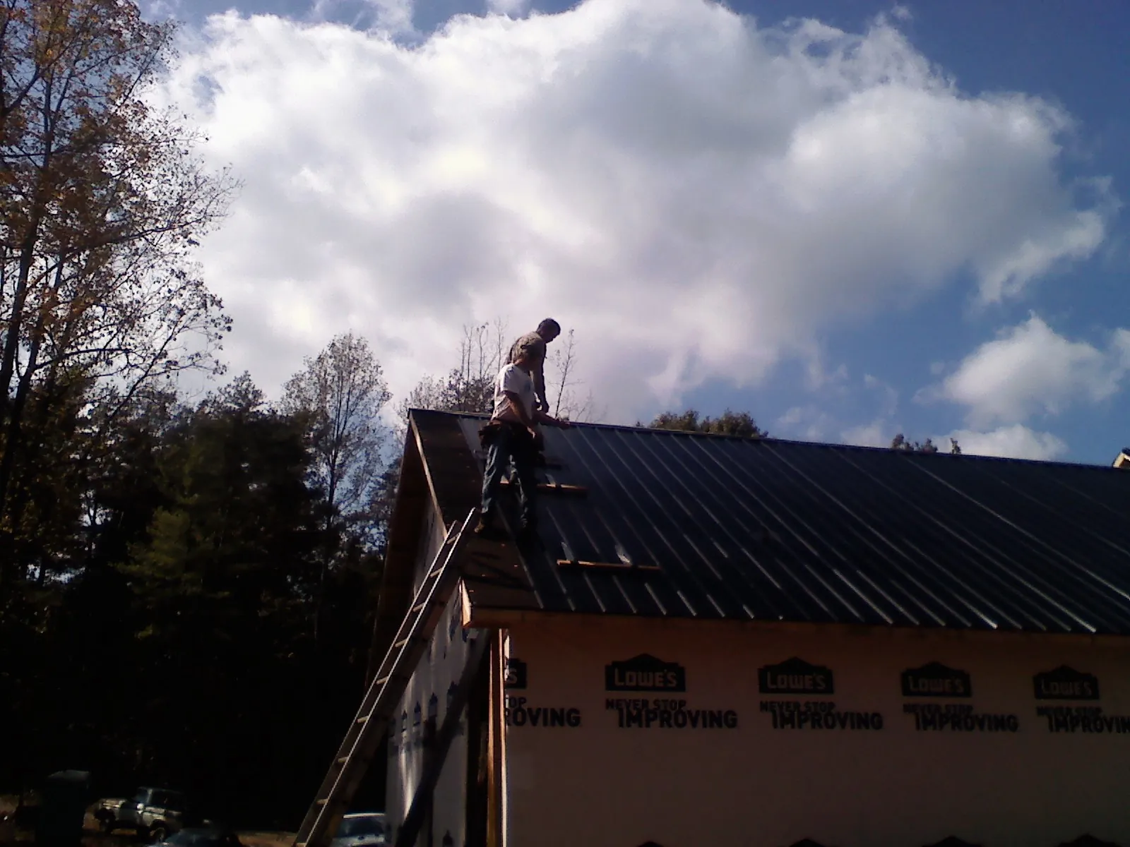 Roofer fastening dark metal panels high against a cloudy sky, from a Roof Inspection job in Liberty Lake