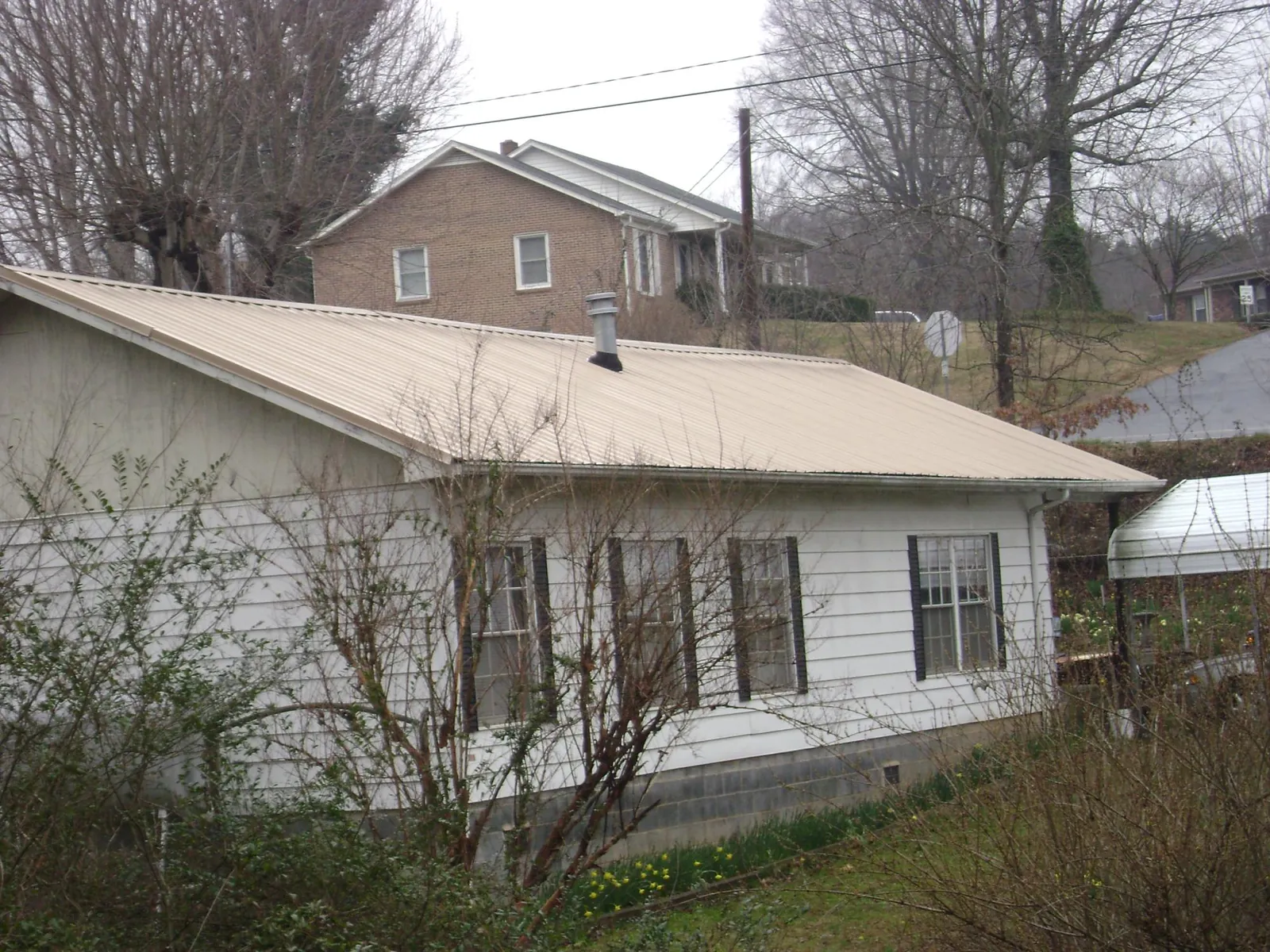 Tan metal roof on a white sided house set into a hillside — Commercial Roofing by Roofing Brothers in Liberty Lake